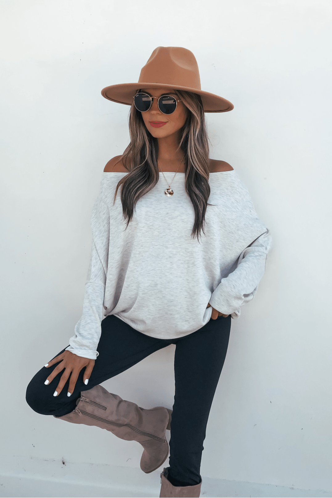 Woman in tan hat and sunglasses poses confidently in a Grey Soft Cloud Scuba Pullover paired with black pants.