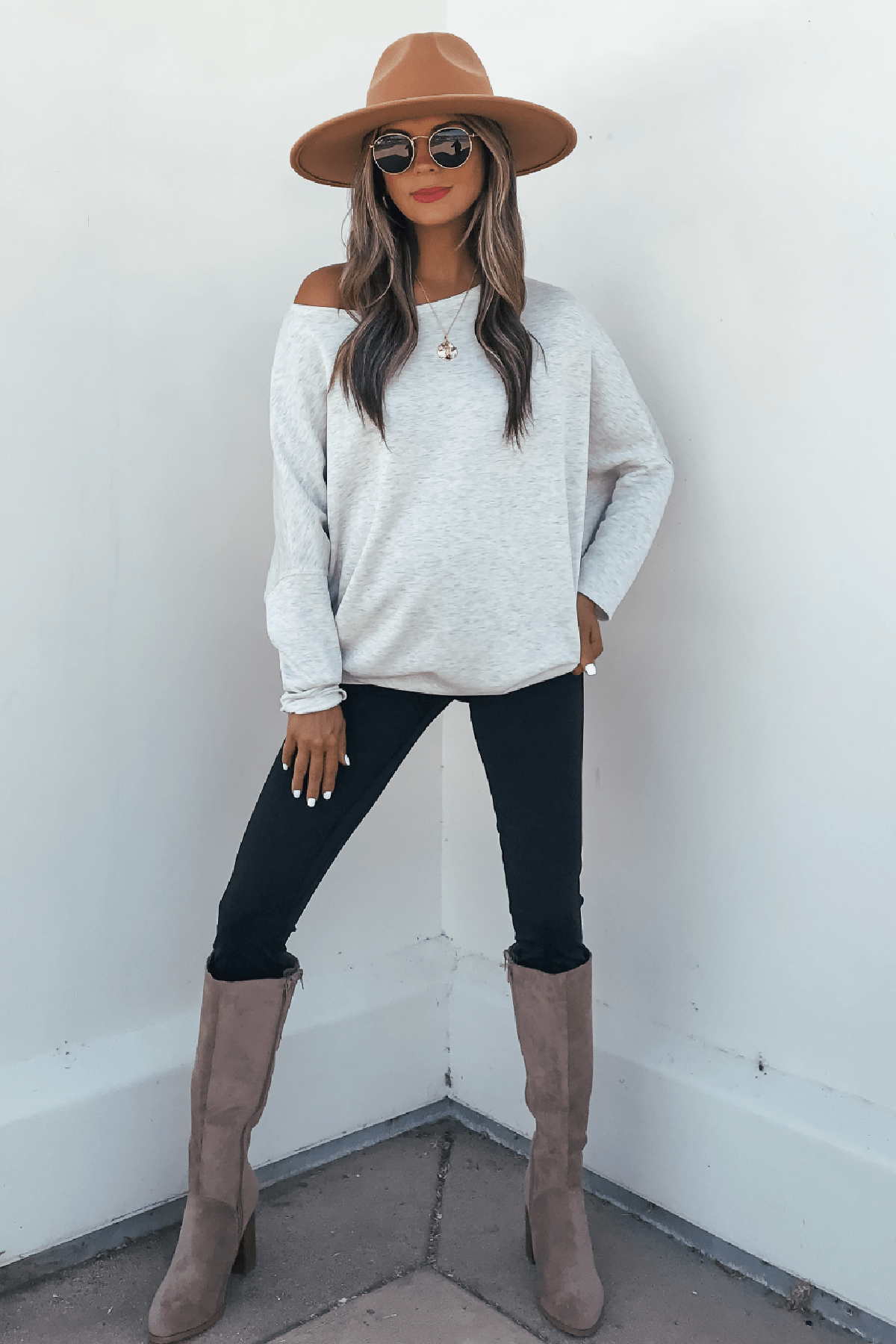 Woman wears a Grey Soft Cloud Scuba Pullover with tan hat, sunglasses, and black pants against a white wall.