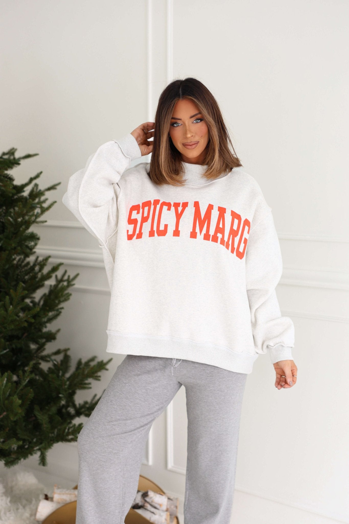 Woman with shoulder-length brown hair wears the Grey Spicy Margs Reversible Sweatshirt and gray sweatpants indoors.
