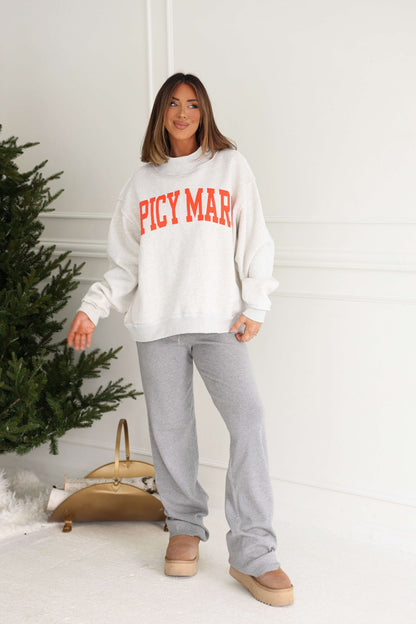 A woman smiles indoors near a Christmas tree, wearing the Grey Spicy Margs Reversible Sweatshirt and gray sweatpants.