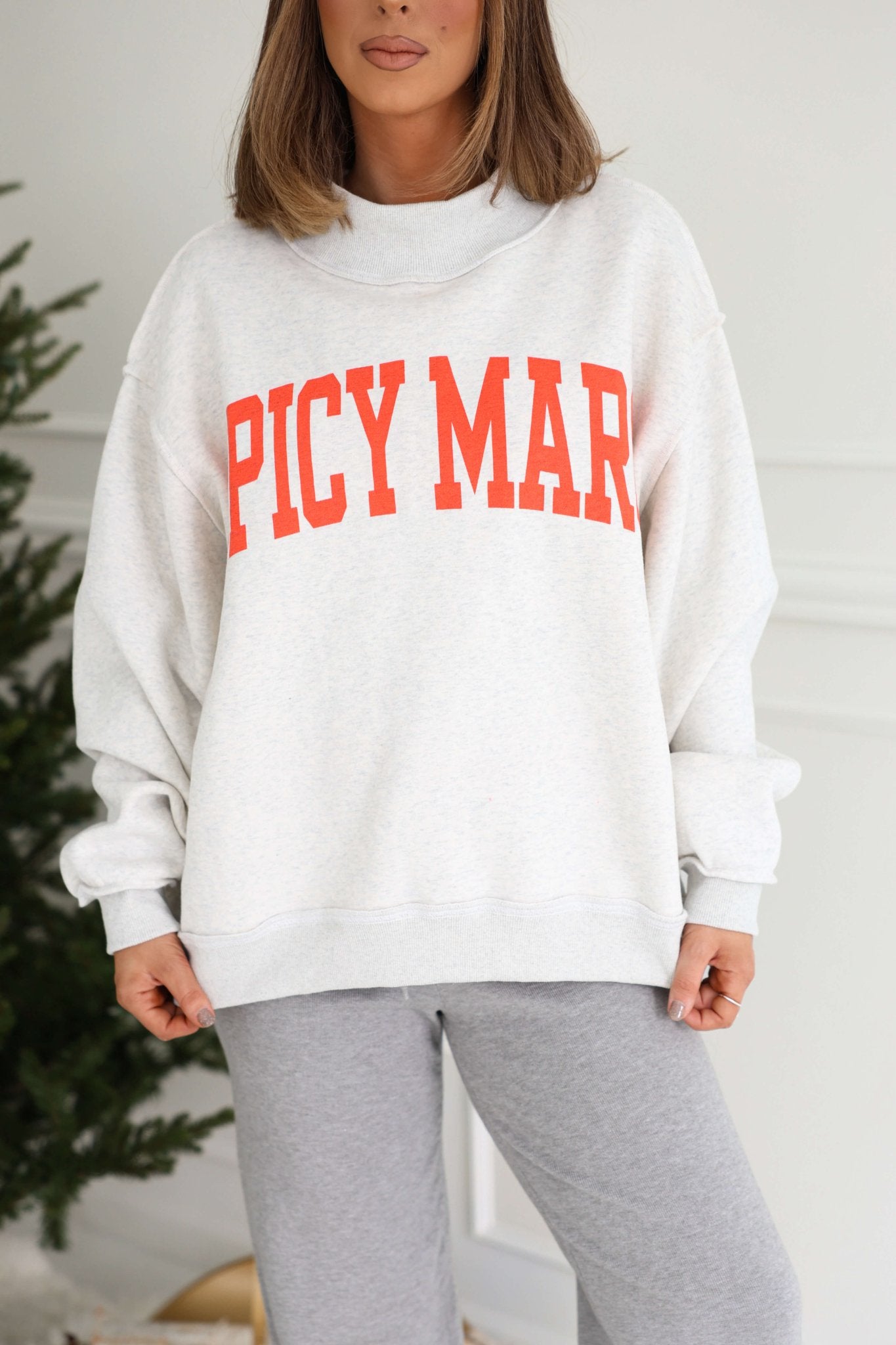 A woman in a Grey Spicy Margs Reversible Sweatshirt and gray pants stands indoors near a green plant.