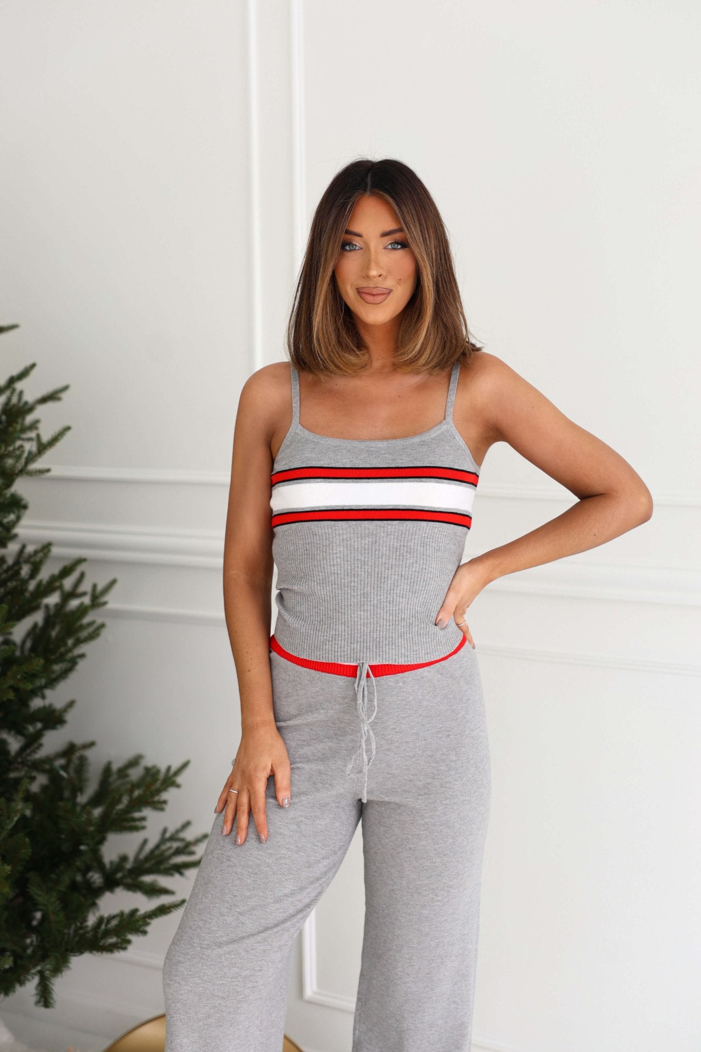 Woman wears Magnolia exclusive Grey Striped Rib Knit Tank Top - FINAL SALE, standing indoors by a green plant, smiling at the camera.