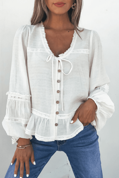 Woman models the Hadley Cream Ruffle Lace Trim Blouse with balloon sleeves, paired with blue jeans against a plain background.