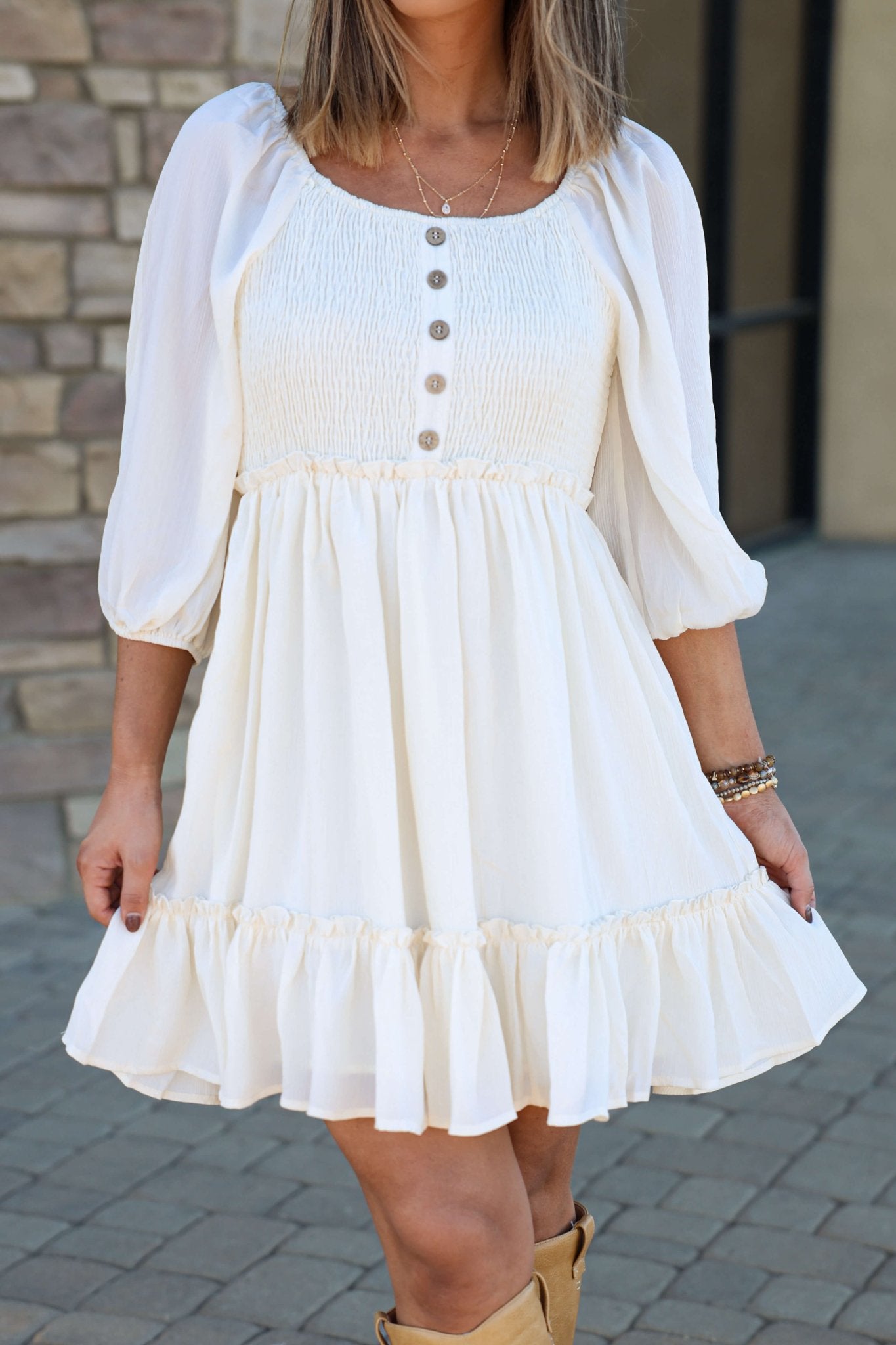 Woman in the Hadley Cream Smocked Mini Dress - DOORBUSTER, with puff sleeves and ruffled hem; chic and bump-friendly.