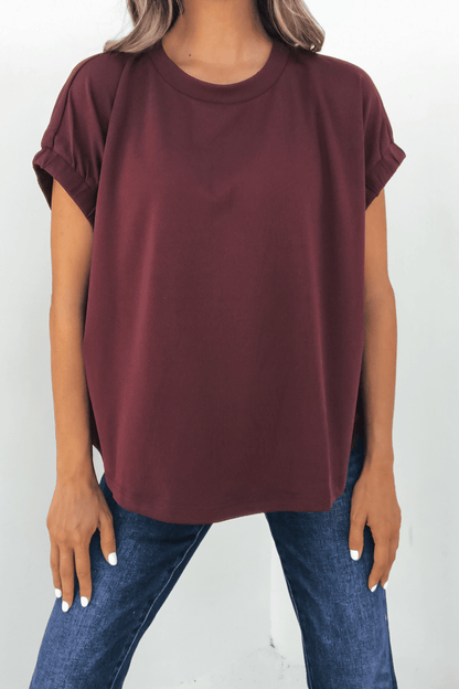 Woman in Harlow Burgundy Short Sleeve Blouse and blue jeans, standing against a white background.