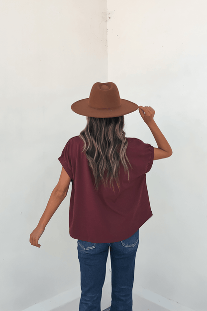 Wearing the Harlow Burgundy Short Sleeve Blouse with blue jeans and a brown hat, she creates an autumn-ready look.