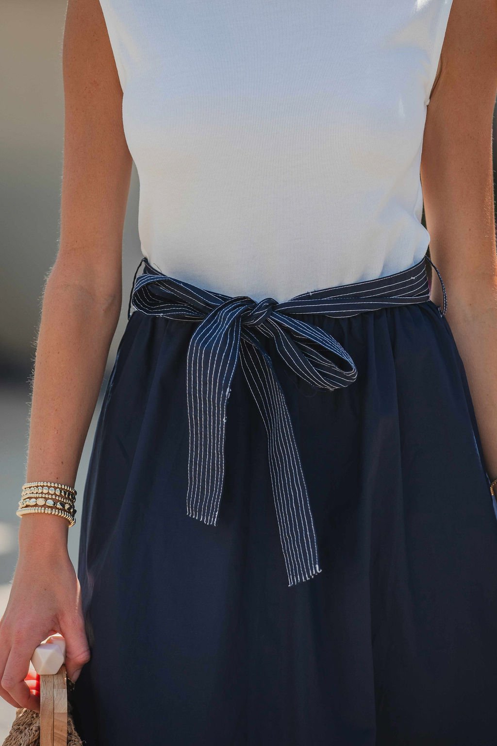 Woman wearing the Hartford Contrast Tie Midi Dress in navy, holding a bag and bracelets on her wrist.