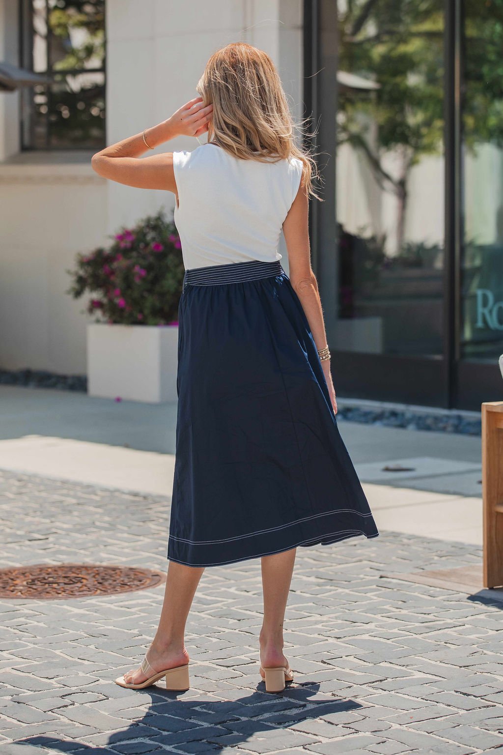 A woman in the Navy Hartford Contrast Tie Midi Dress stands outdoors on a cobblestone street, facing away with one hand on her head.