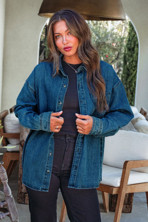 Woman with long brown hair wears the Harvest Blues Dark Denim Shacket indoors near wooden chairs and plants.