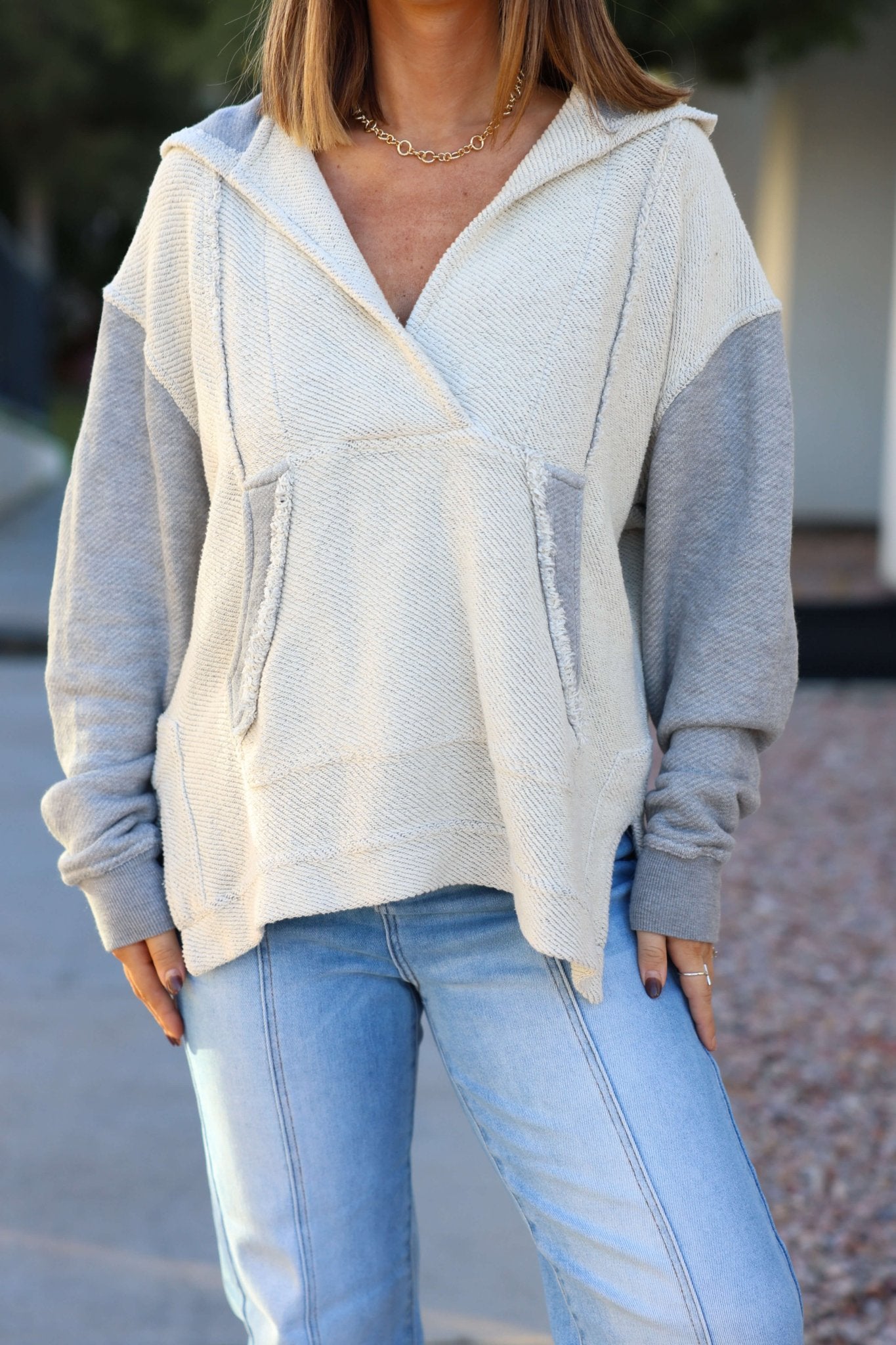 A woman wears a Heather Grey Slouchy Hooded Sweatshirt with front pockets and light blue jeans while standing outdoors.