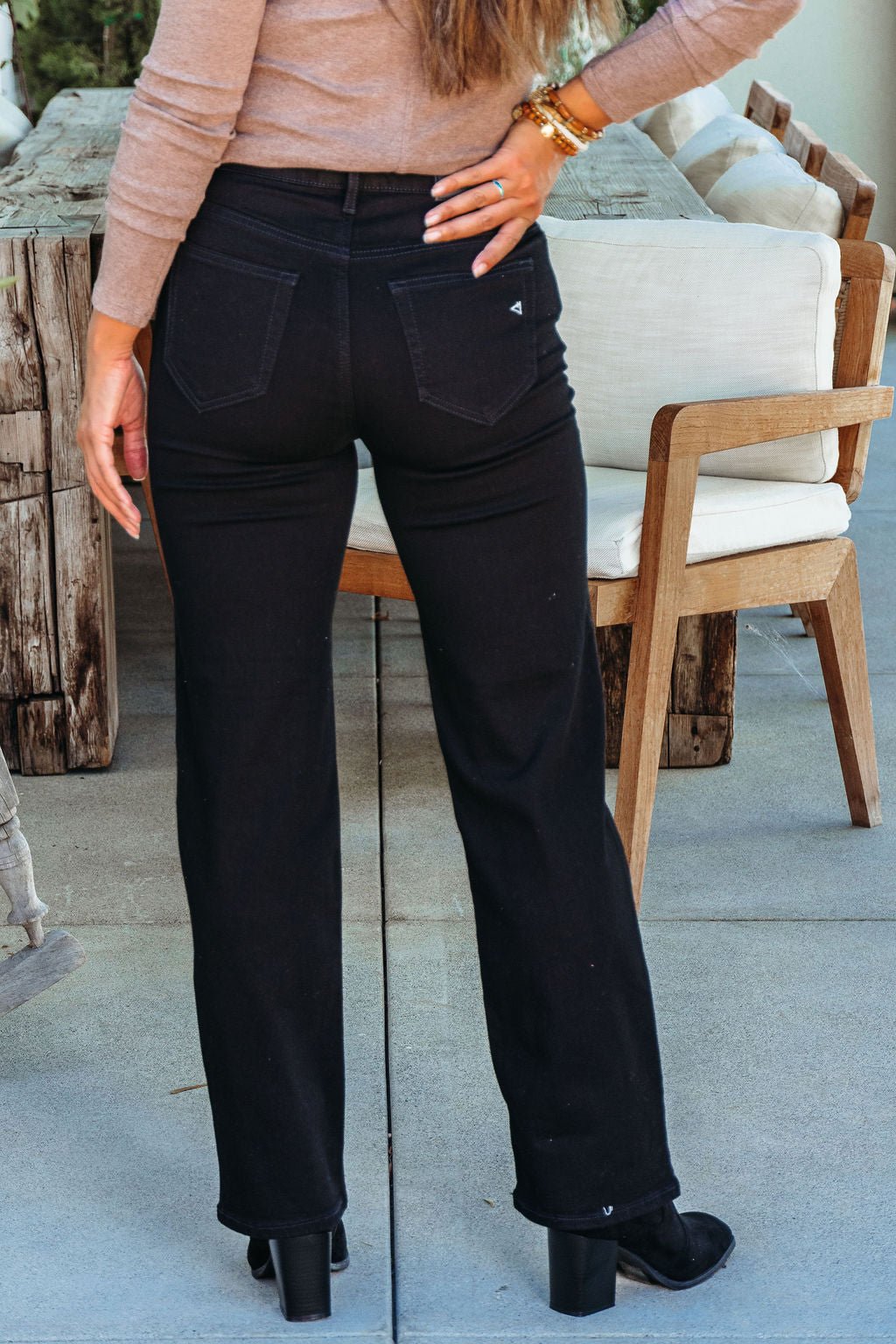 Woman stands outdoors in Hidden Black High Rise Straight Leg Jeans and heeled boots, hand on hip near a wooden table.