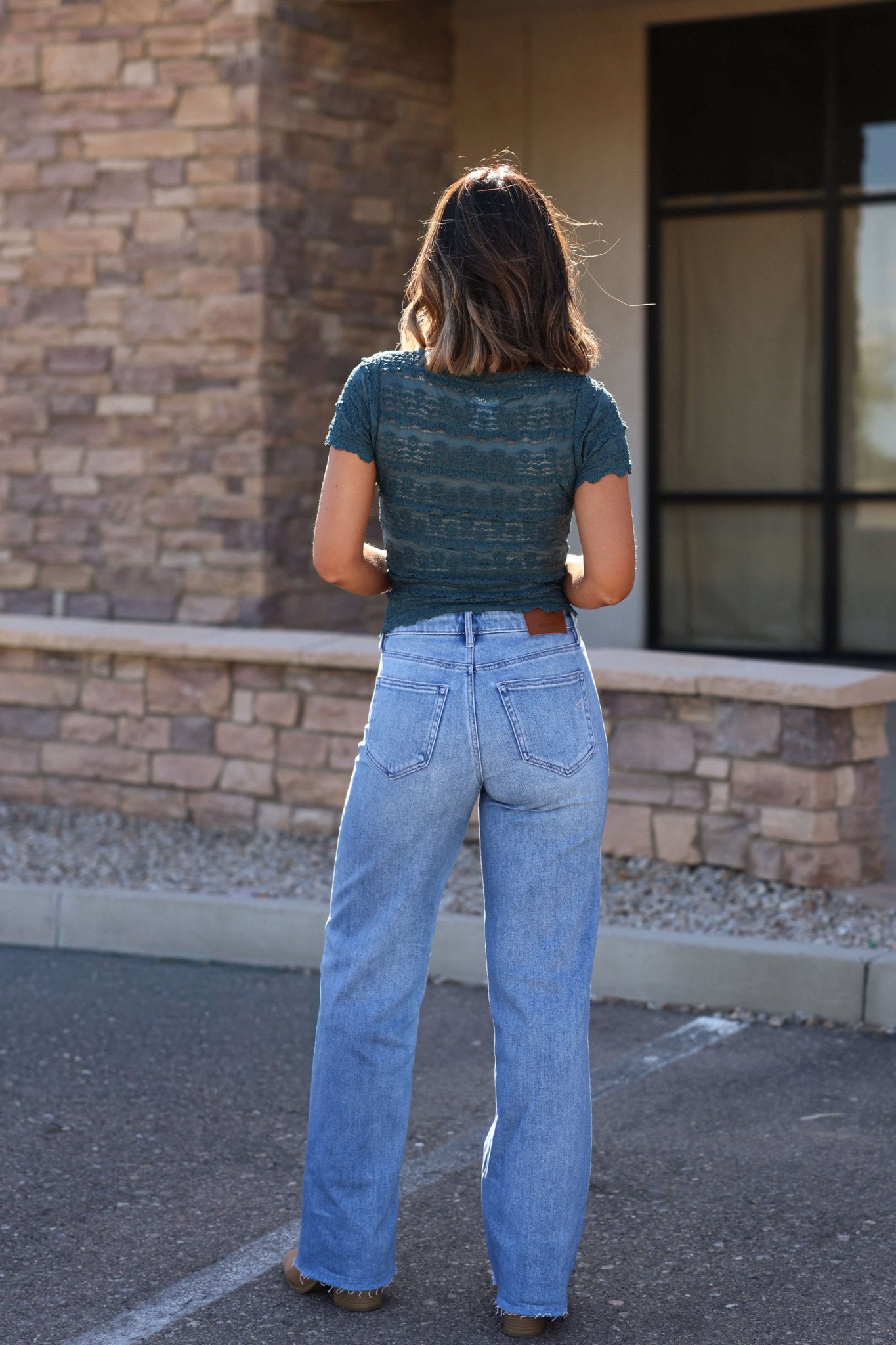 A woman in a green top and Hidden Light Wash Basic Dad Jeans stands outside, facing away from the camera.