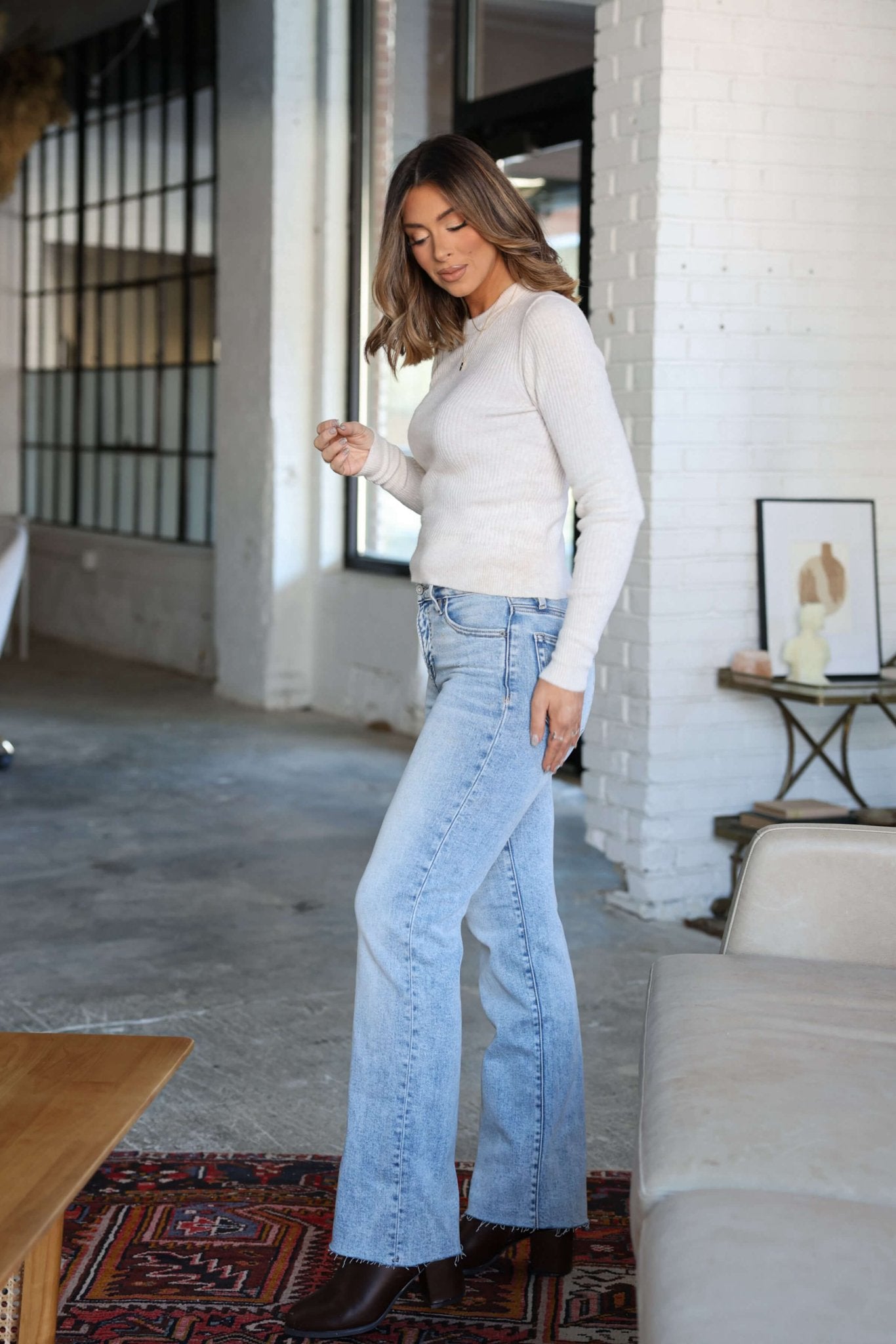 A woman in a white top and Hidden Light Wash Straight Leg Jeans stands in a sunlit room with industrial-style windows.