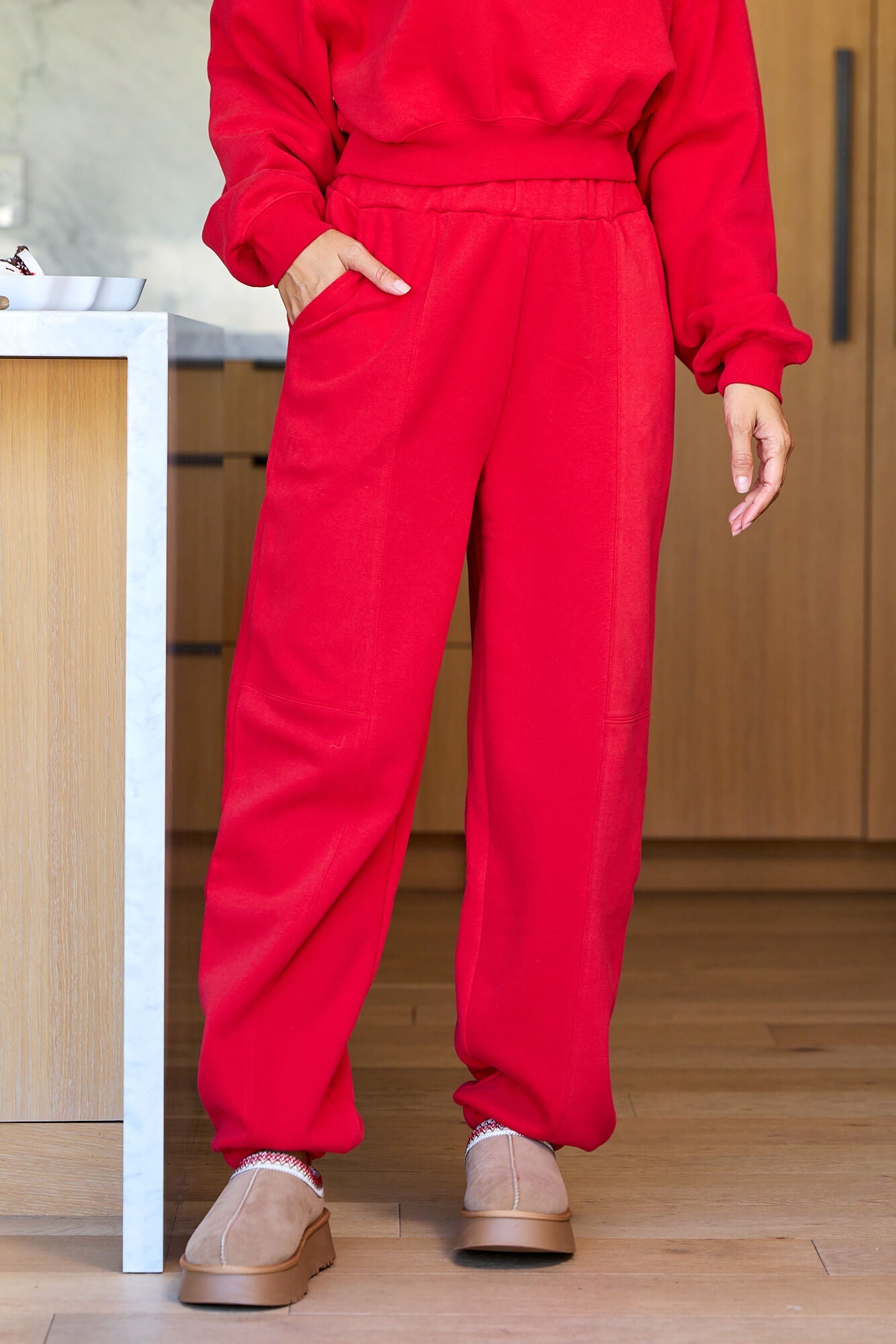 Wearing Holiday Red Lounge Jogger Sweatpants - FINAL SALE with a matching top and tan slippers in a modern kitchen.