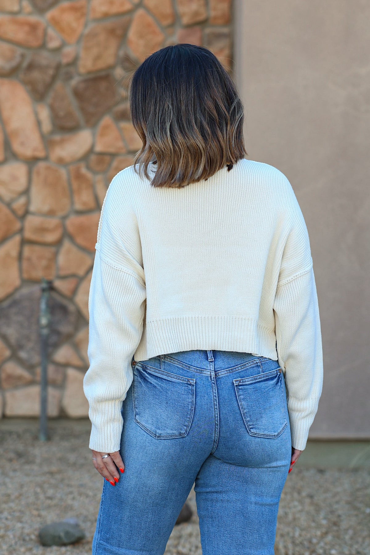 Woman with shoulder-length hair wears the HYFVE DZ26C982 cream drop shoulder sweater, standing outdoors with her back to the camera.