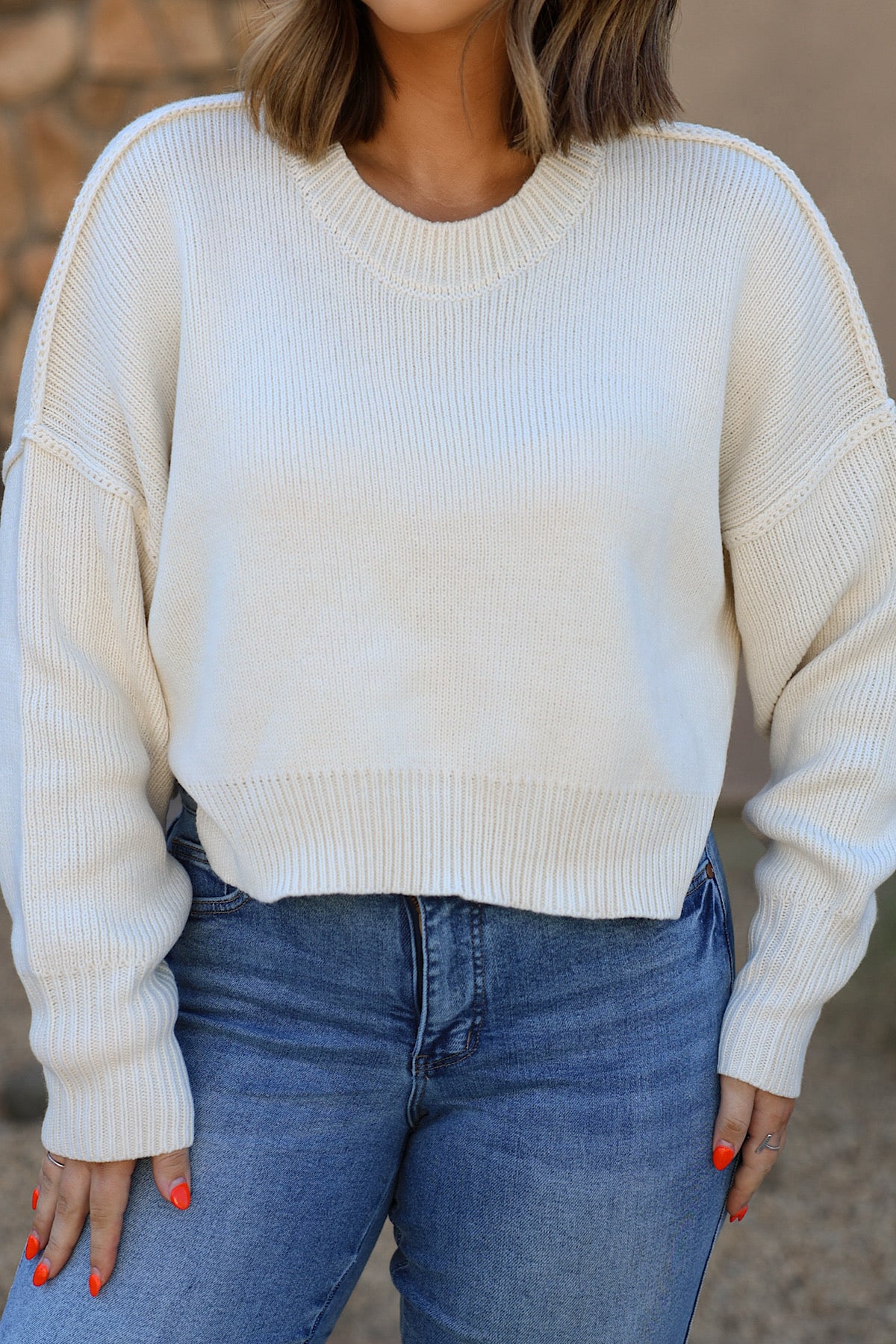 Woman wearing HYFVE DZ26C982 cream long sleeve drop shoulder sweater with blue jeans, standing outdoors.