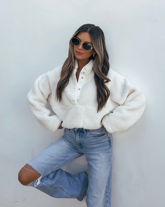A person wearing a white Half ZIP Sherpa Jacket and light-wash distressed jeans.