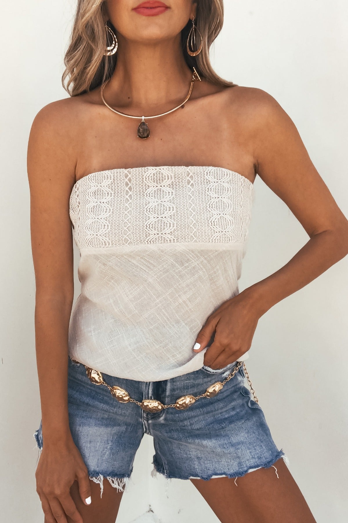 Woman wearing the Isla Natural Lace Tube Top, denim shorts, gold jewelry, and a chain belt against a plain background.