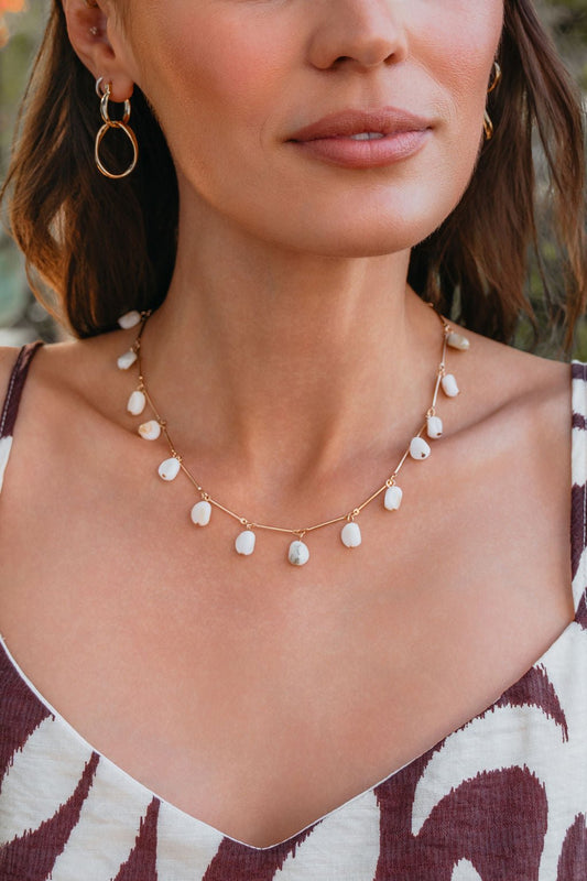 A woman wears the Isla Pearl Beaded Necklace, a gold-tone chain with pearl beads, paired with a patterned top.