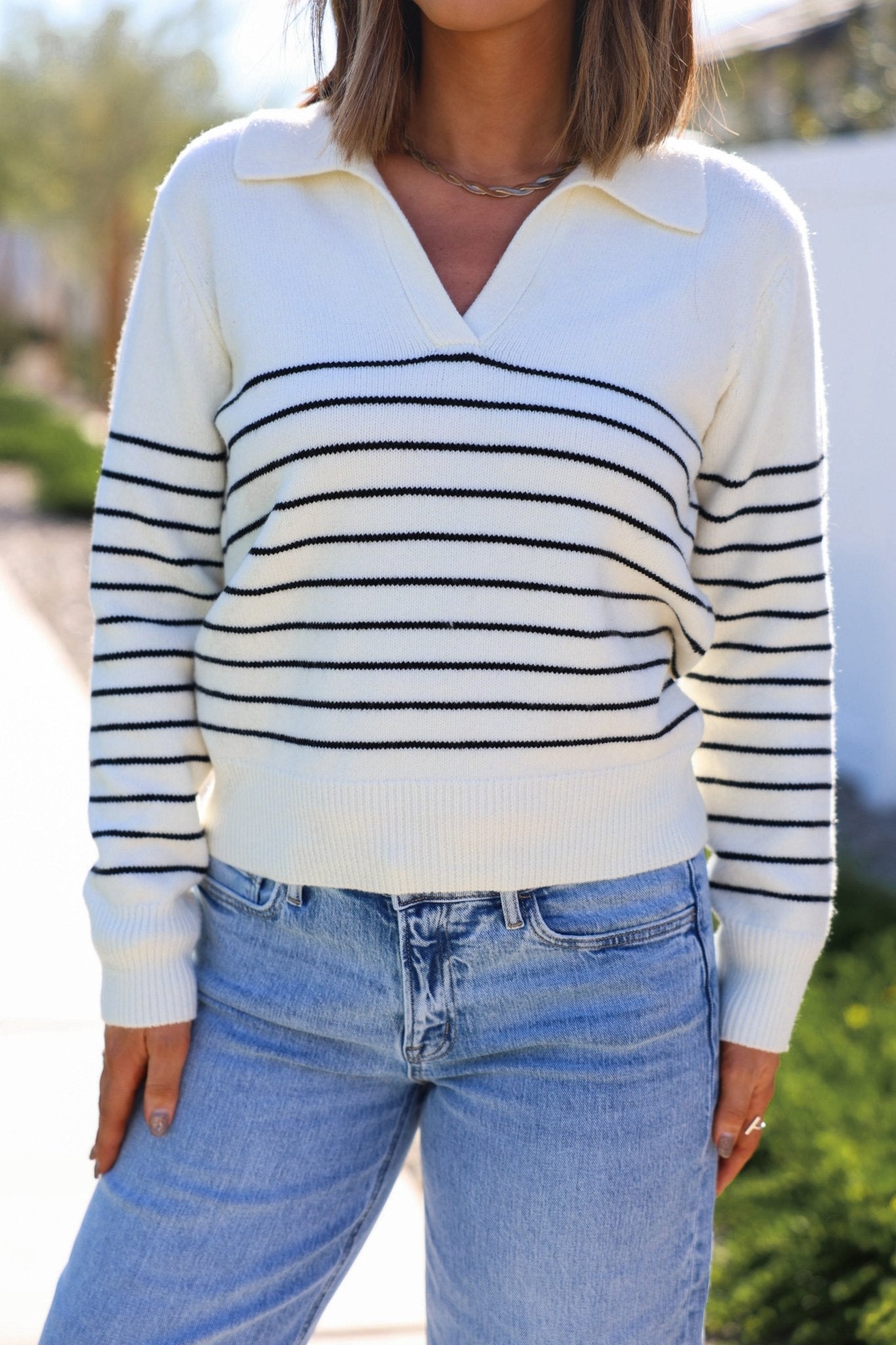 A person outdoors wears the Ivory and Black Stripe Ribbed Sweater with light blue jeans, ideal for a chic winter look.