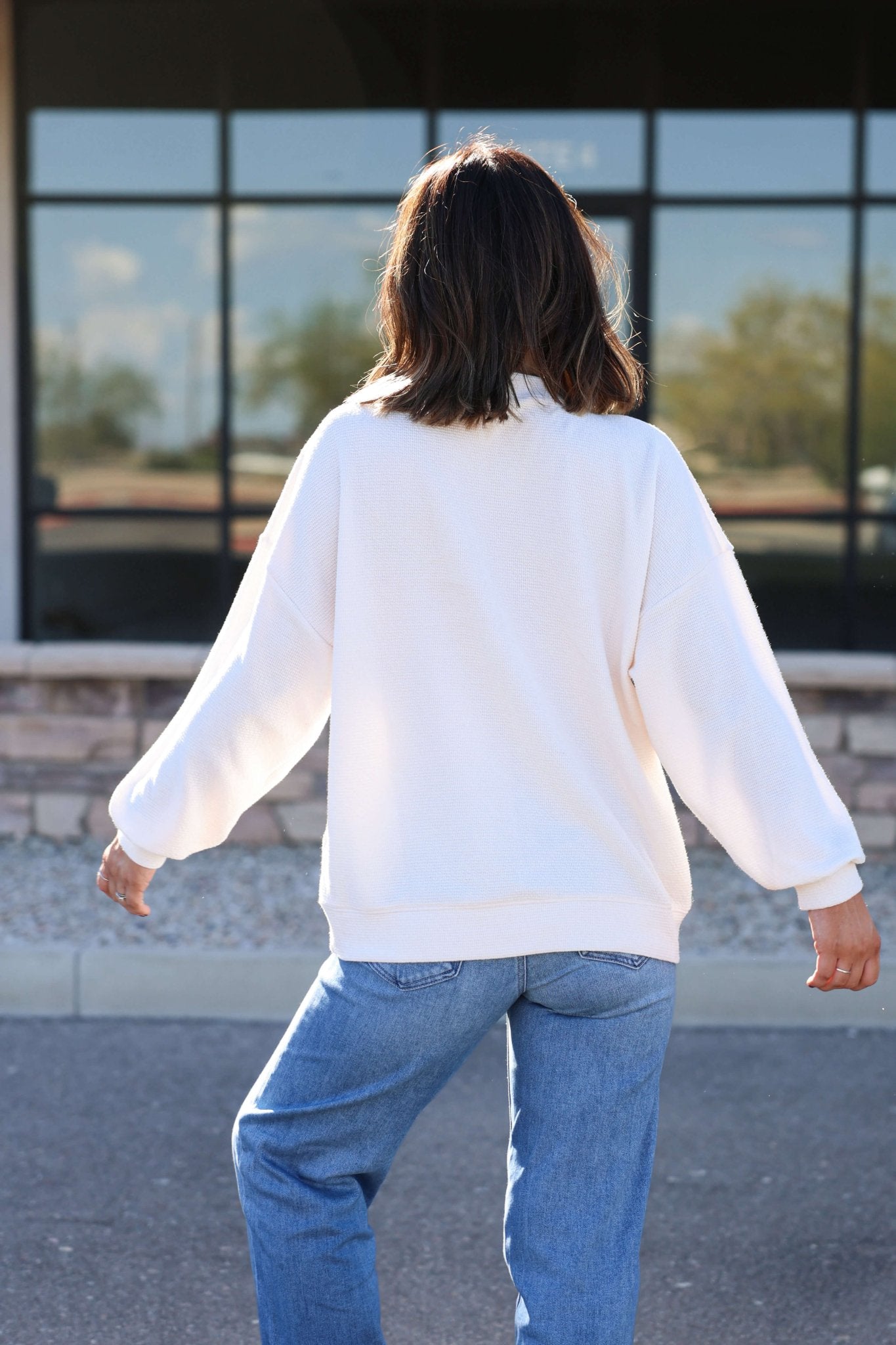 Someone stands outdoors in an Ivory and Red Indiana Graphic Pullover and blue jeans, showing casual Hoosier pride.