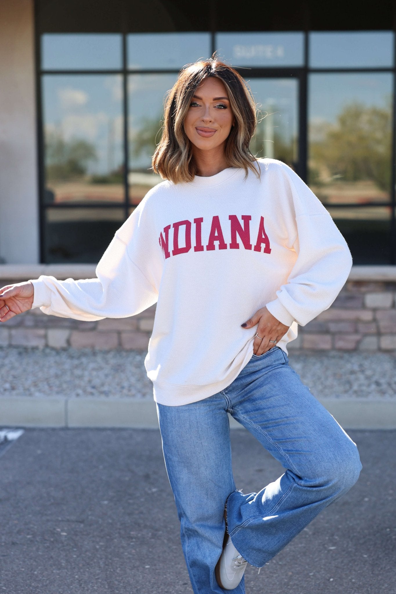 Woman smiles outdoors in an ivory and red Indiana Graphic Pullover, blue jeans, and shows her Hoosier pride.