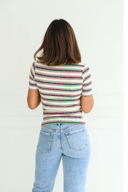 A woman with shoulder-length brown hair models the Ivory Contrast Striped Rib Polo Top, standing with her back to the camera.