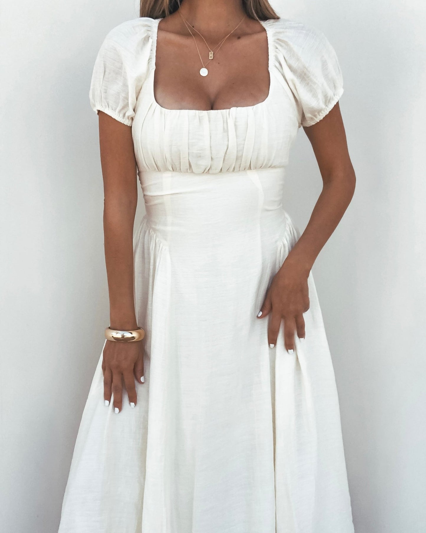 Woman in an Ivory Puff Sleeve Shirred Midi Dress with a gold necklace and bracelet, standing against a white background.