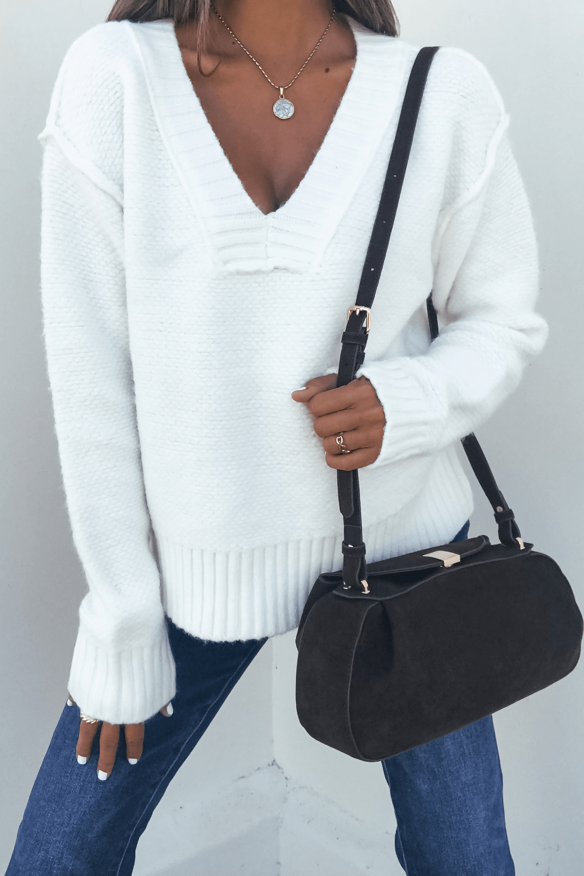 A person wearing an Ivory Seam Detail Ribbed Sweater, blue jeans, a necklace, and carrying a black shoulder bag.