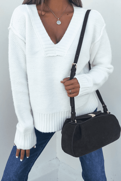 A person wearing an Ivory Seam Detail Ribbed Sweater, blue jeans, a necklace, and carrying a black shoulder bag.