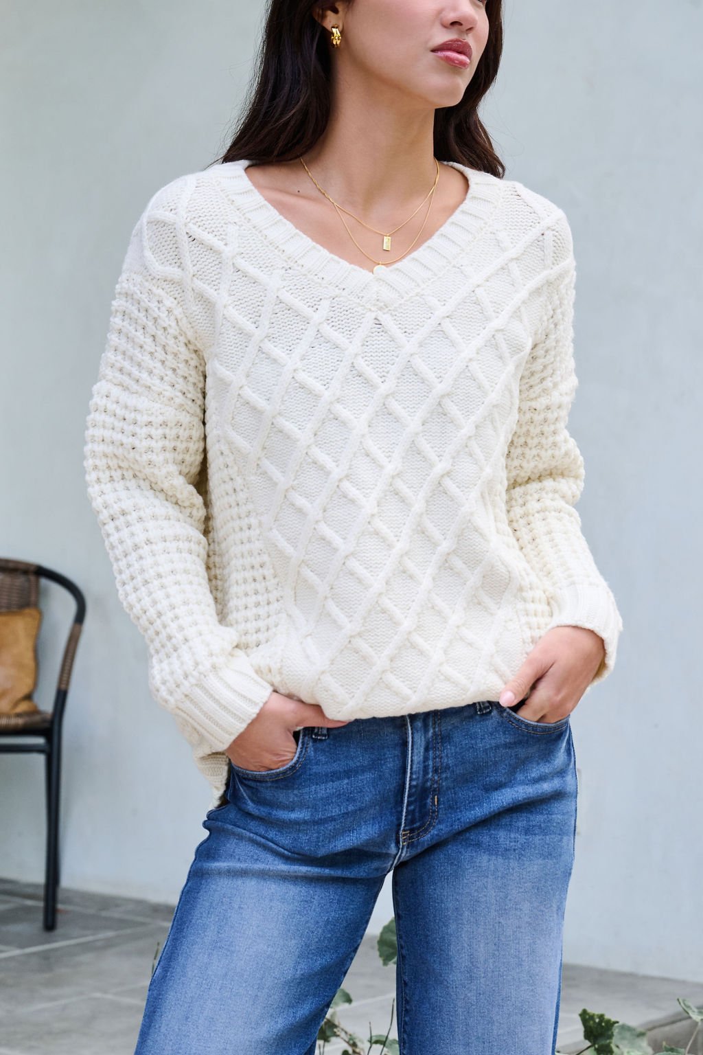 Woman models the Ivory Textured Cable Knit Sweater with blue jeans, standing hands in pockets against a minimal neutral backdrop.