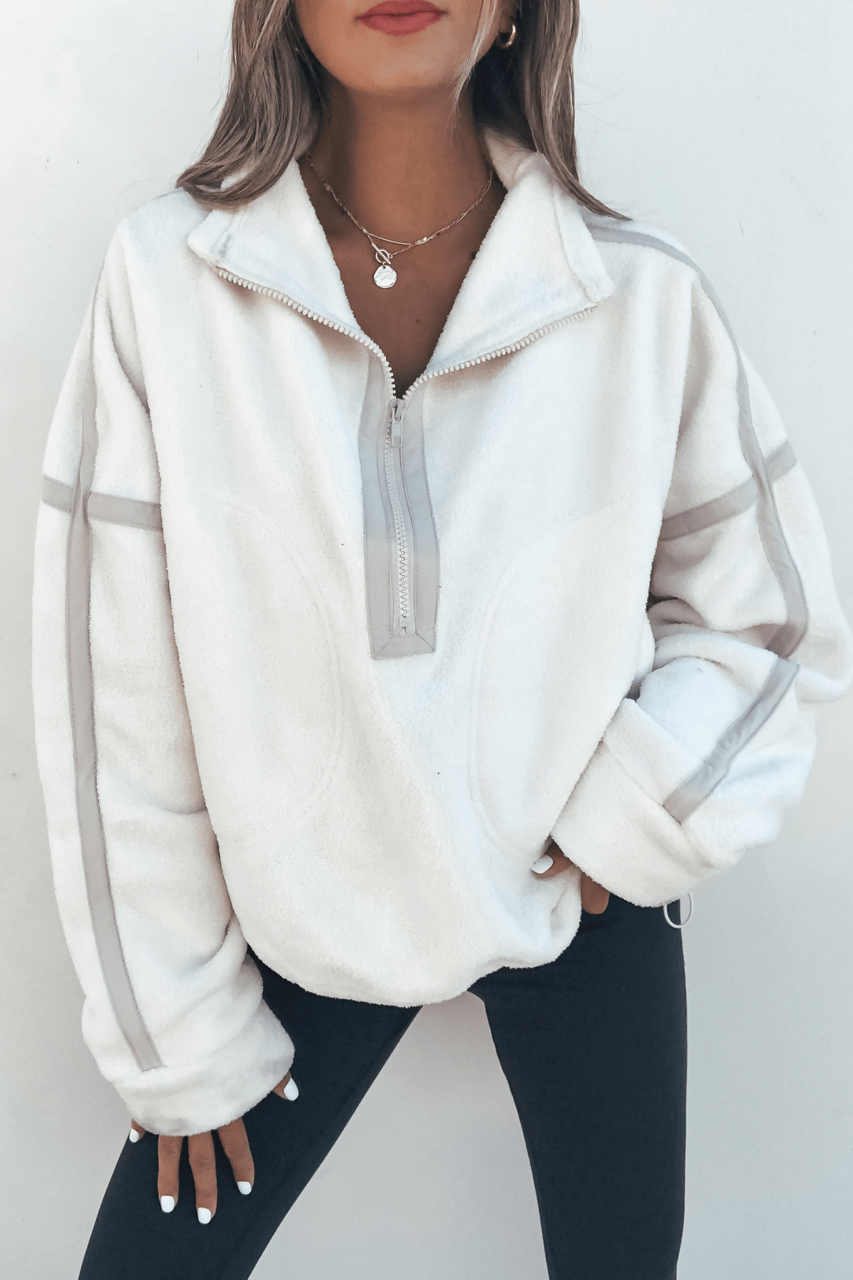 Woman in Ivory Trim Detail Half Zip Sweatshirt and black leggings, standing with one hand on her hip against a plain background.