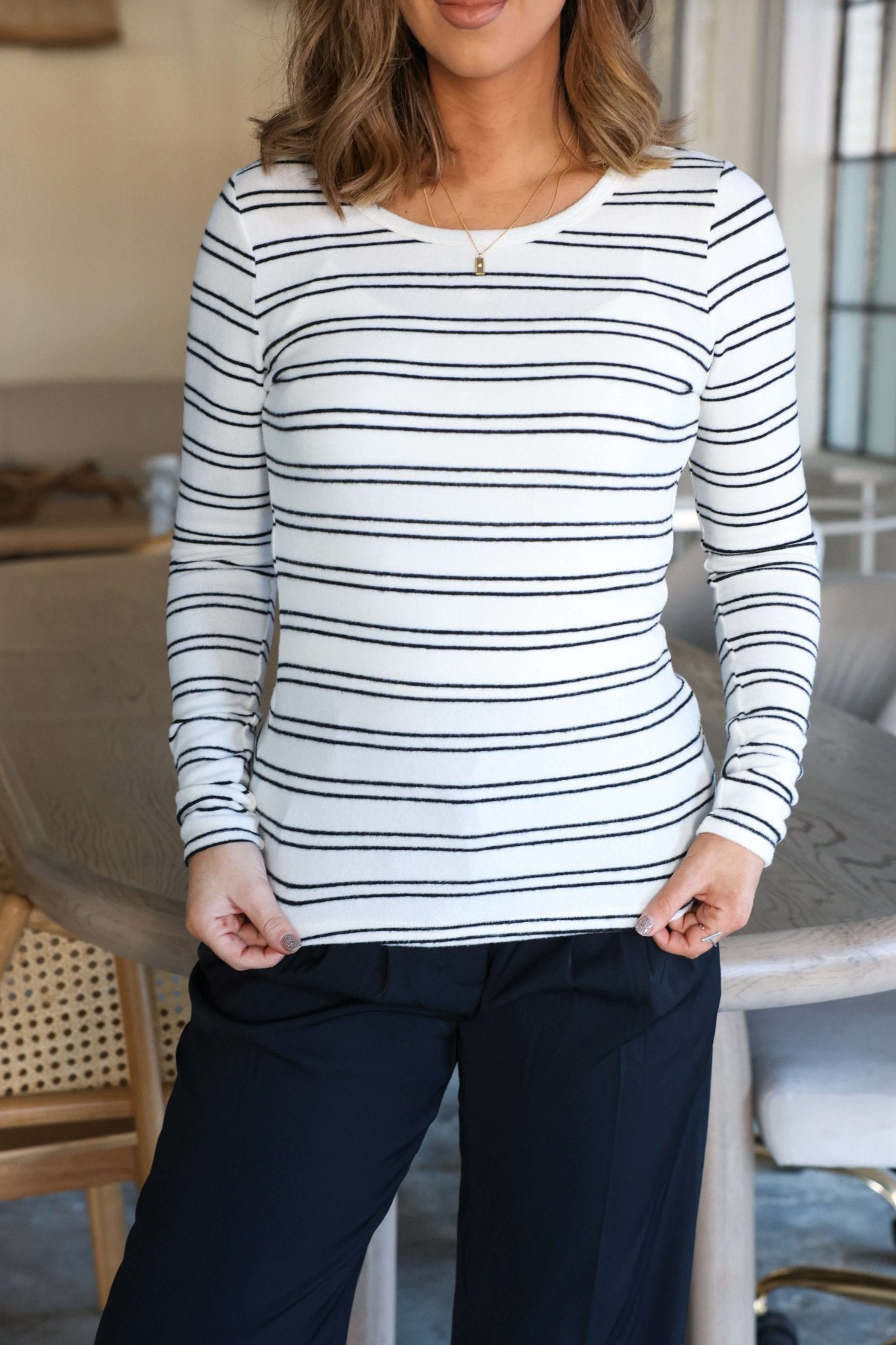 Woman in a Jenna Black and White Double Stripe Top with black pants, standing casually indoors.