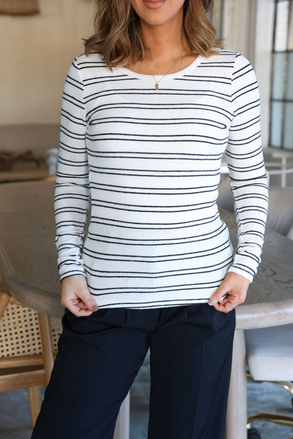 Woman in a Jenna Black and White Double Stripe Top with black pants, standing casually indoors.