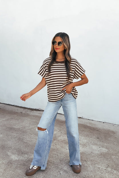 Woman in sunglasses wears the Joan Striped Knit Top - Brown, ripped wide-leg jeans, and sneakers against a white wall.