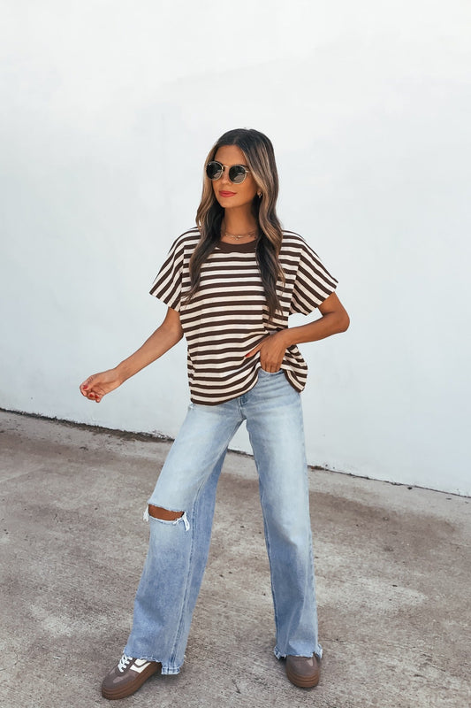 Woman in sunglasses wears the Joan Striped Knit Top - Brown, ripped wide-leg jeans, and sneakers against a white wall.