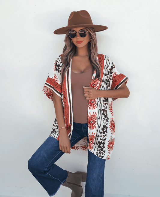 Woman in sunglasses, brown hat, blue jeans, boots, and a Jolene Multi Red Border Print Kimono Top posing against a white background.