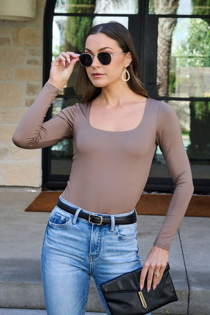 A woman in sunglasses and blue jeans stands outdoors holding a black clutch, wearing the Jordan Mocha Square Neck Bodysuit.