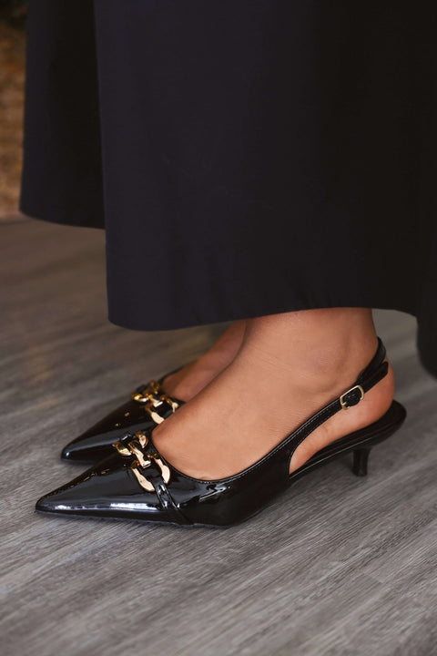 Someone stands elegantly on a wooden floor wearing the Josephine Black Slingback Kitten Heels - FINAL SALE.
