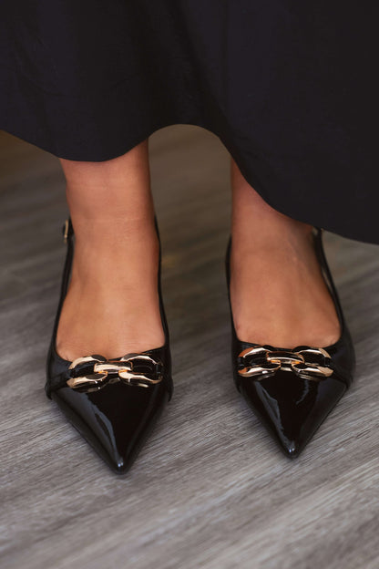 A person wearing Josephine Black Slingback Kitten Heels stands on a wooden floor.