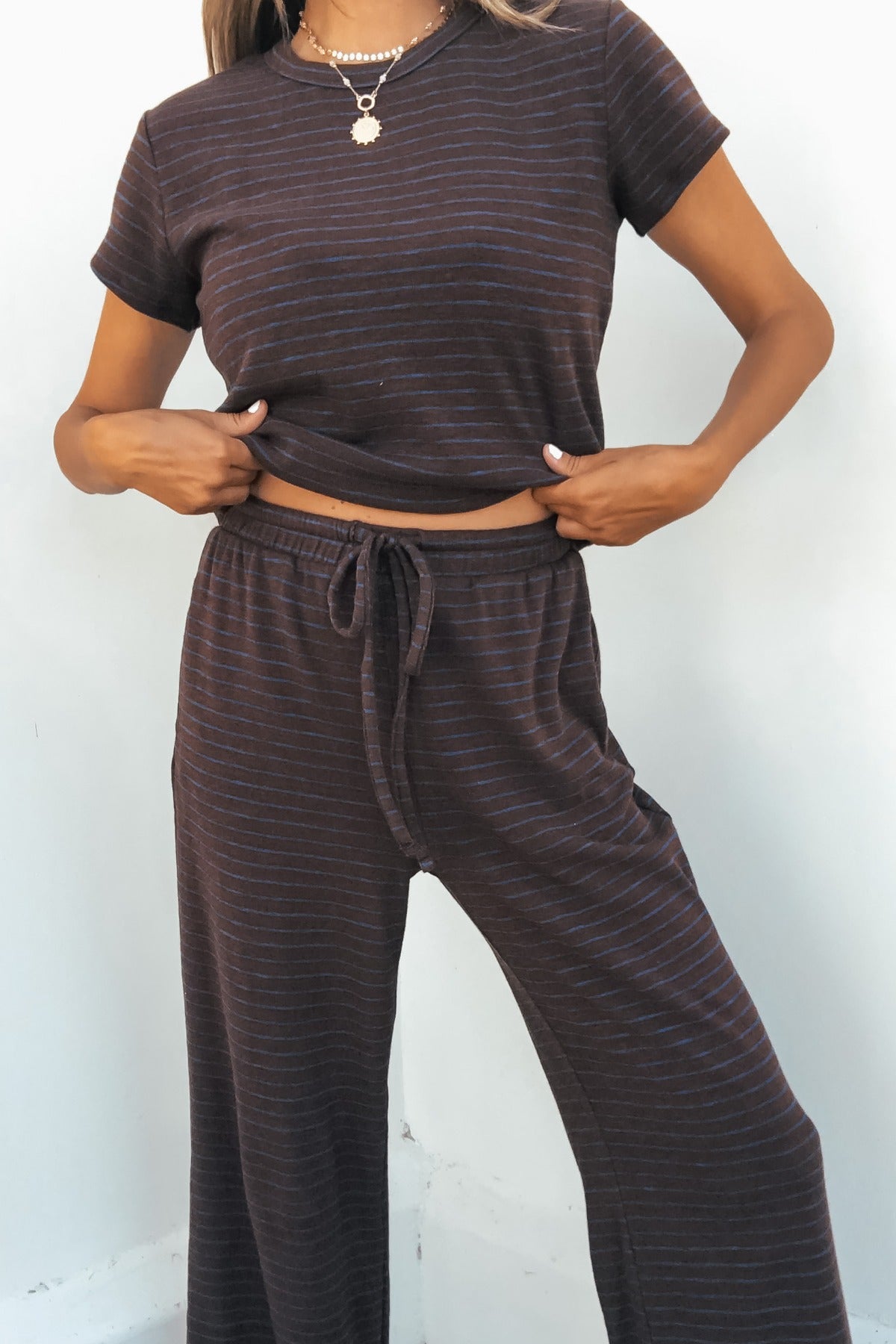 Person wears brown Kacey Striped Wide Leg Pants with an elastic waistband, slightly lifting a dark striped tee to show the fit.