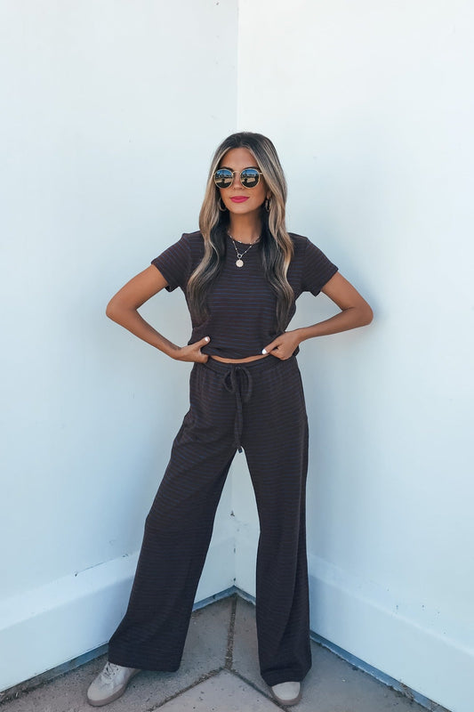 Woman wears Kacey Striped Wide Leg Pants in brown, sunglasses, and a matching set, standing confidently against a white wall.