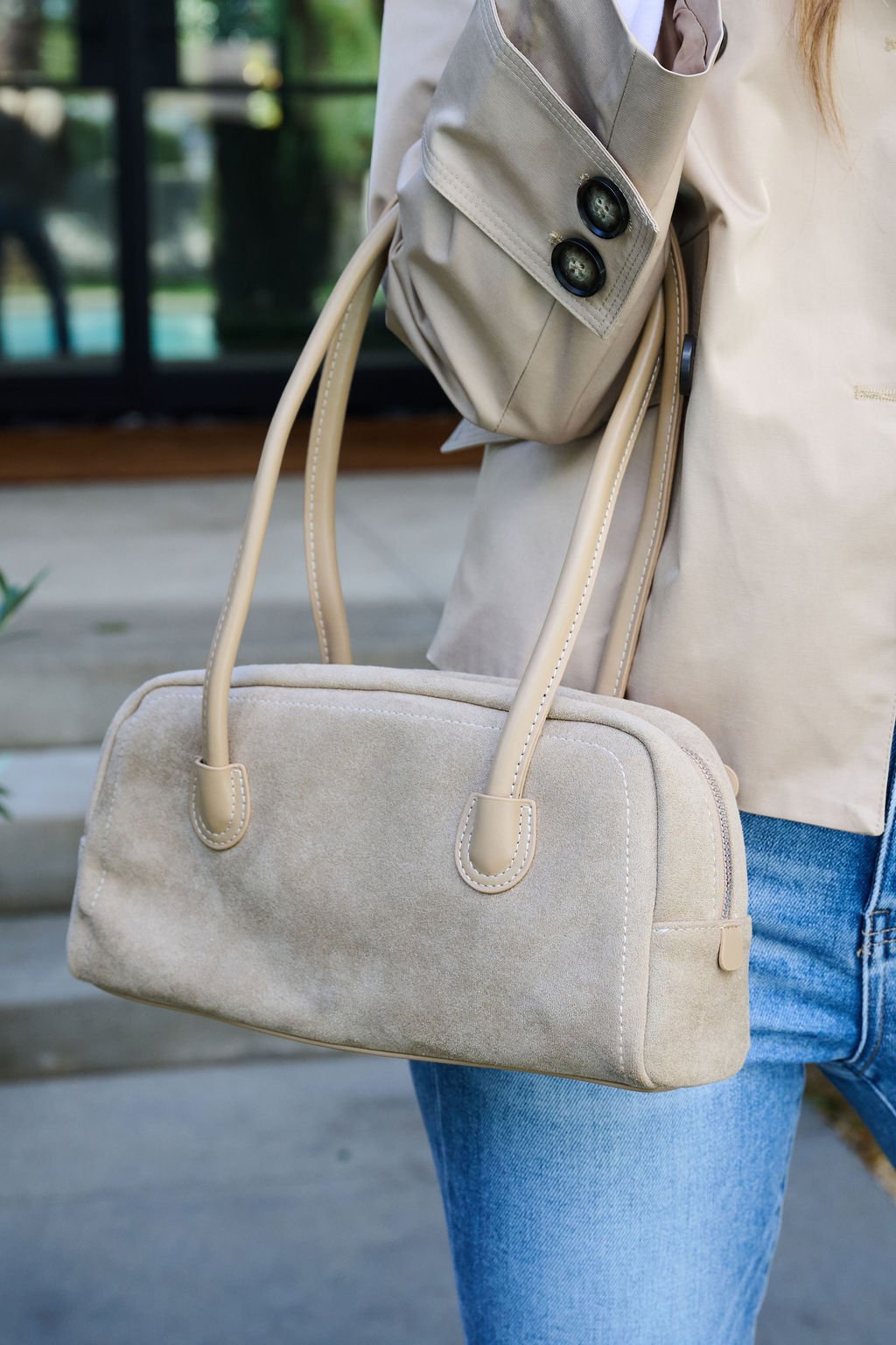 A person outdoors holds the Khaki Faux Suede Baguette Bag, styled with two handles, paired with a beige jacket and jeans.
