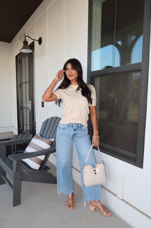 Woman stands on a porch in the Kiersten Champagne Short Sleeve Sweater - FINAL SALE, paired with light blue jeans and nude heels.