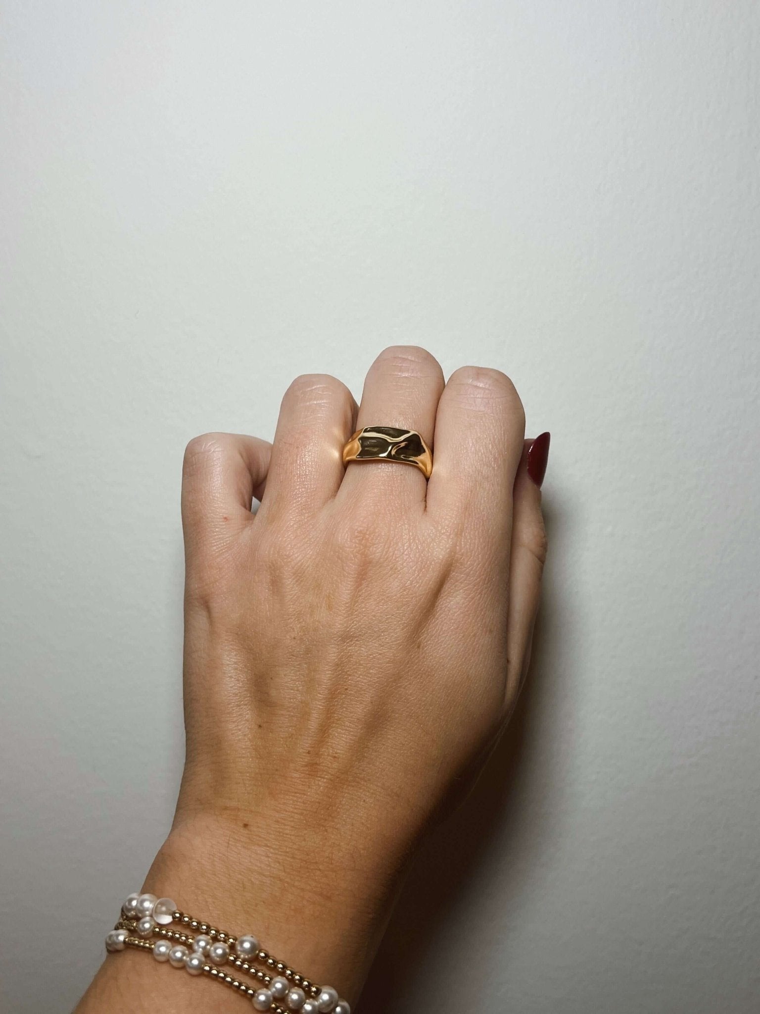 A hand wears the Kinsey Designs Sybil Gold Molten Ring and pearl bracelets against a plain white background.
