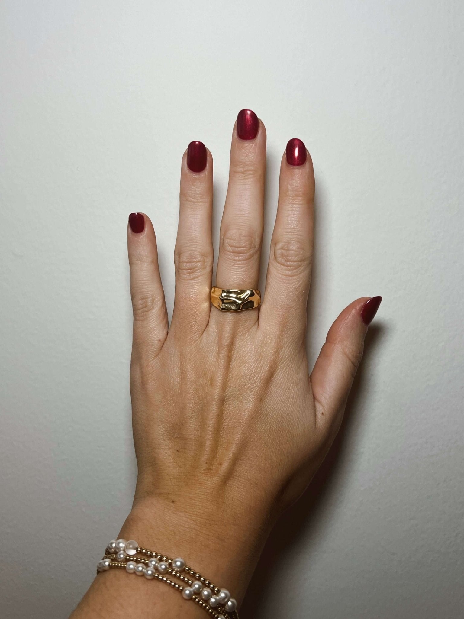 A hand with dark red nails wears the Kinsey Designs Sybil Gold Molten Ring against a plain white background.