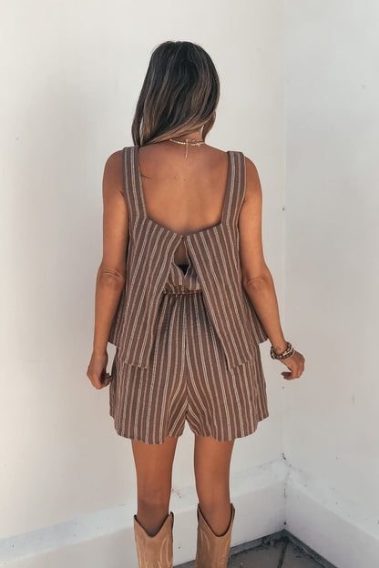 Woman facing away in the Kinsley Brown Pinstripe Romper and tan cowboy boots, standing indoors.