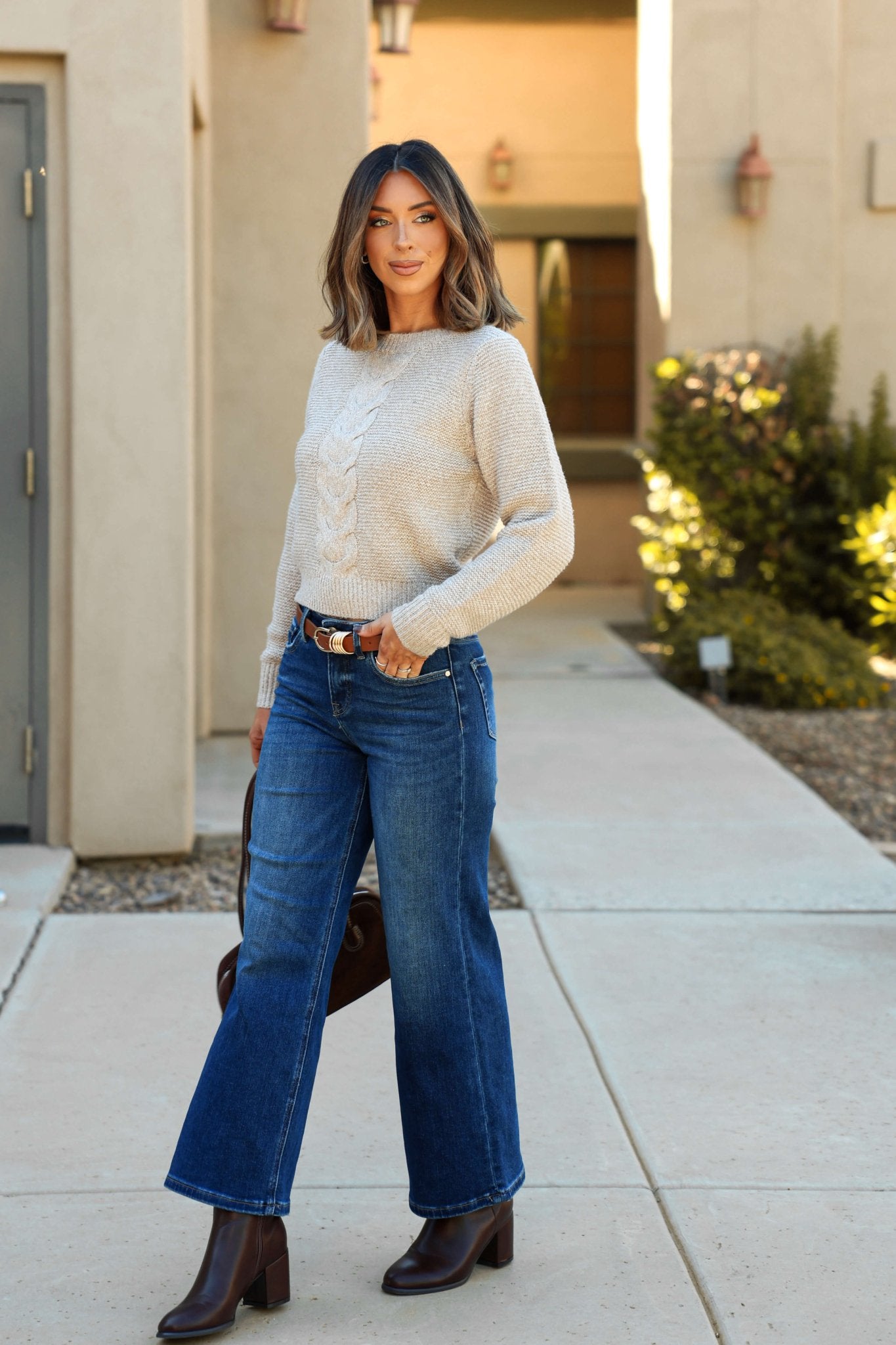 Woman wearing the Kylie Mocha Cable Knit Sweater, wide-leg jeans, and boots stands on a city sidewalk with relaxed style.