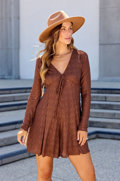 Woman in a brown Lace Tie Romper stands outdoors near steps, looking to the side, wearing a tan wide-brim hat.