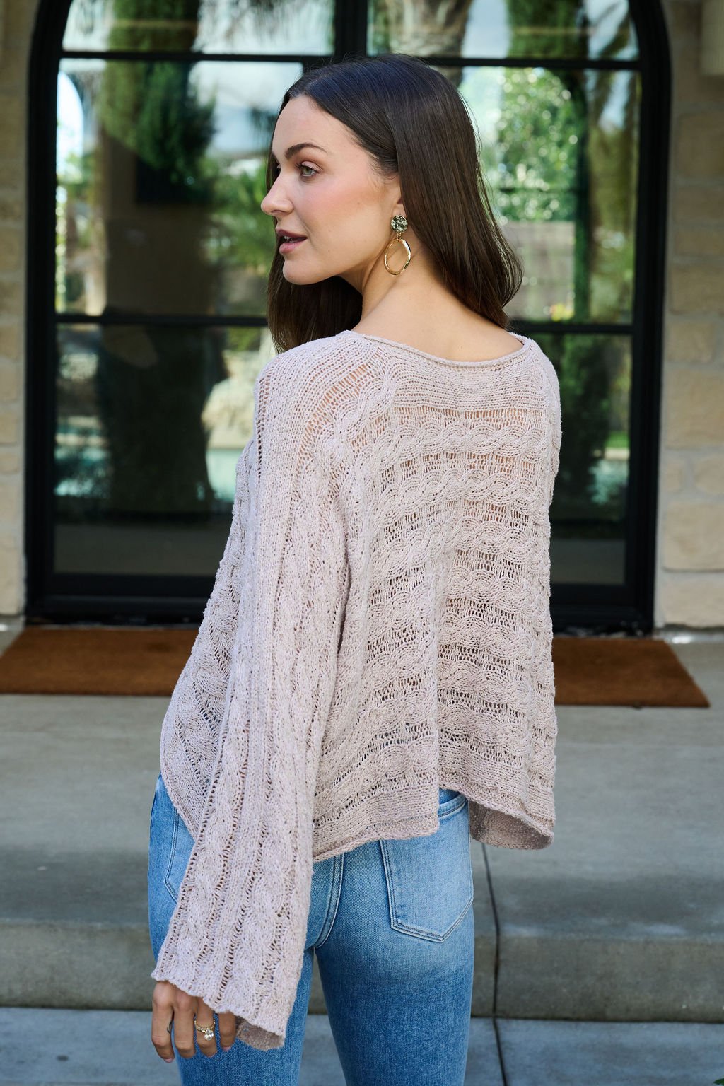 Woman wearing the Laurel Taupe Open Knit Sweater stands outside, looking over her shoulder.